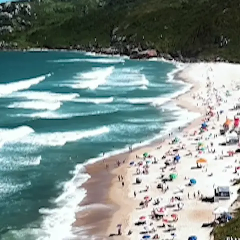 Praia Mole vista de cima, com ondas, guarda-sóis na areia e o morro verde
