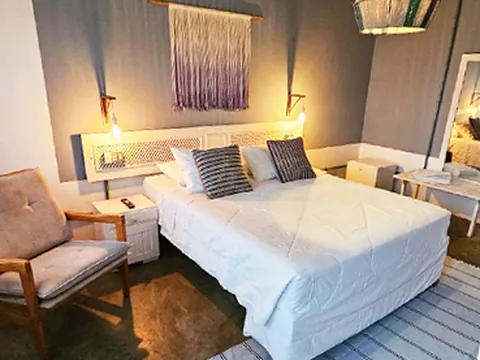 Quarto com cama de casal, macramê na parede e poltrona
